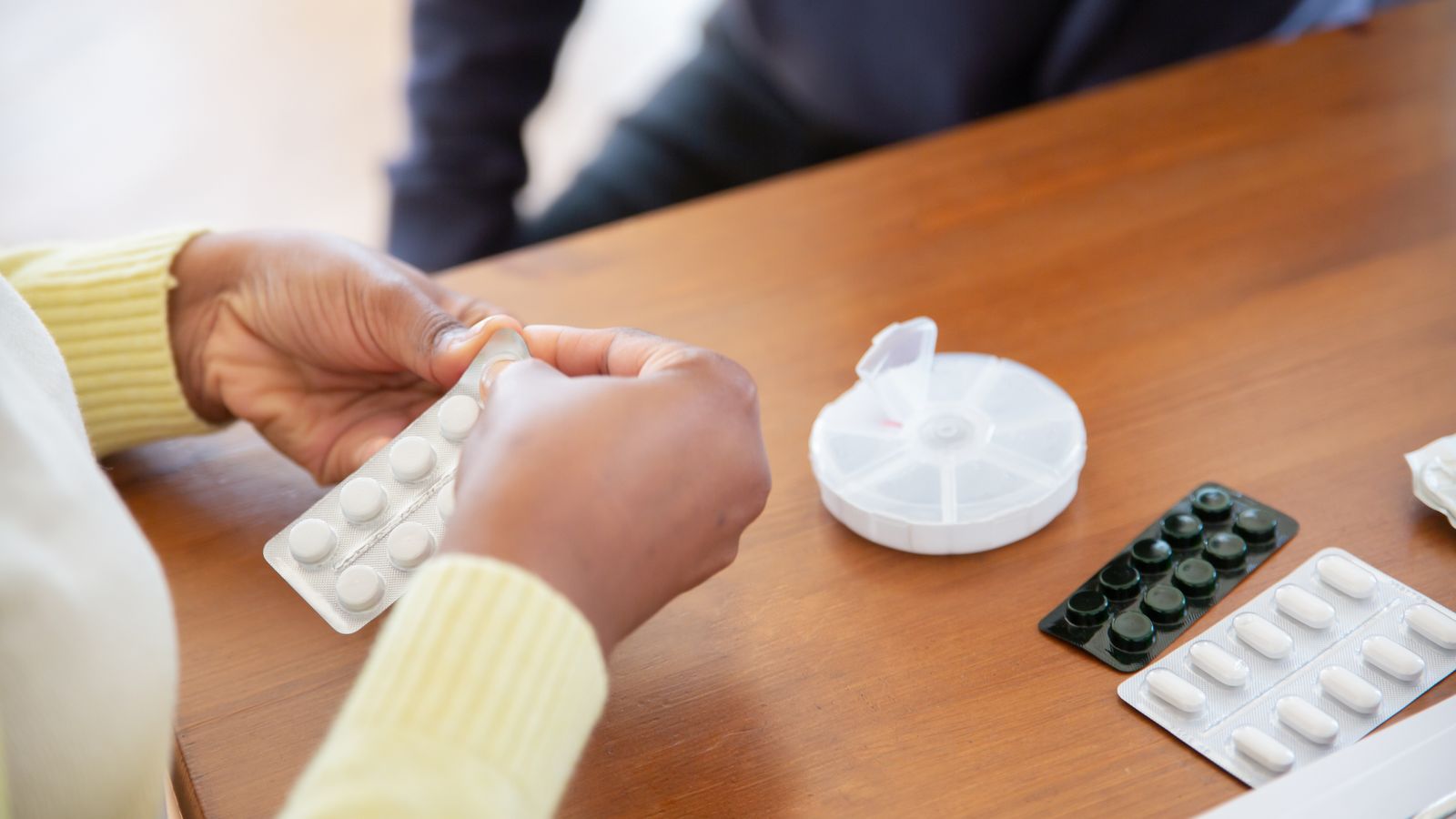 Tablets being pressed from a blister pack beside a weekly pill organiser