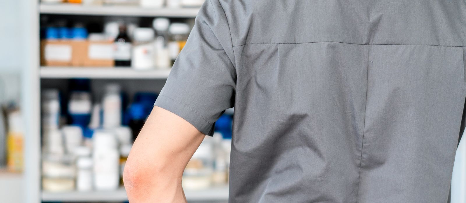 A pharmacist facing a cabinet stocked with medications