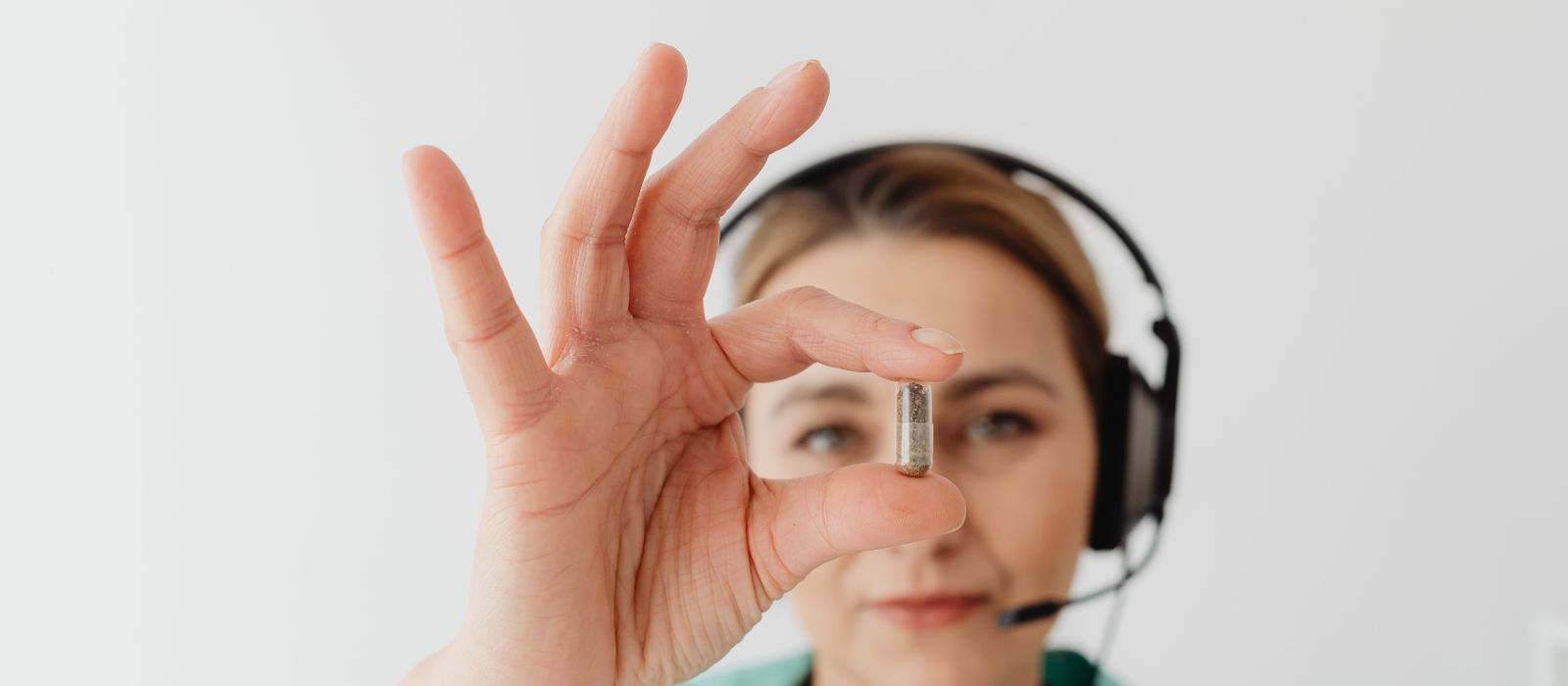 A pharmacy call operator wearing a headset, holding a capsule